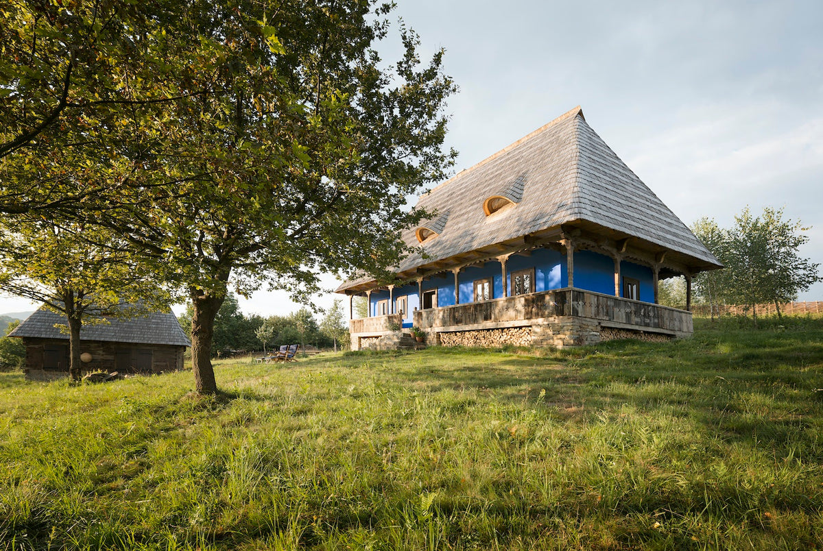 Casa Catuna, traditionally plastered with loam and painted blue, sits in a meadow with cherry, plum, and apple trees. Beside it stands a traditionally furnished barn. Discover more in Slow Escapes.