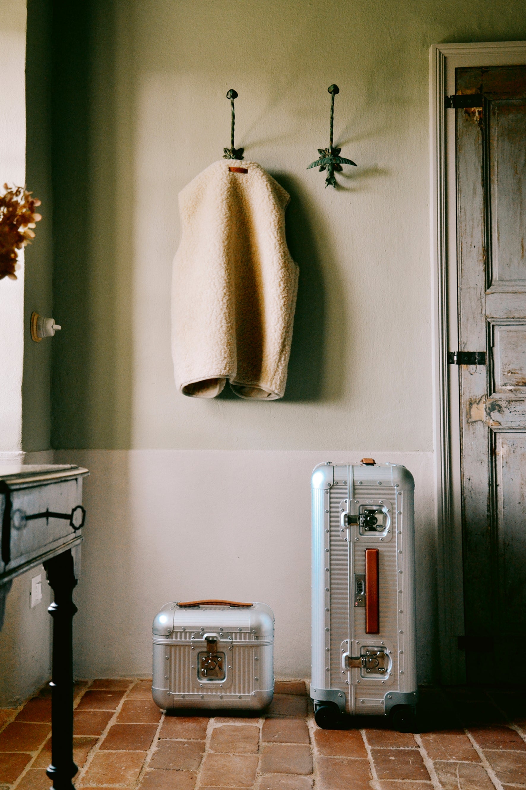 Two vintage-style suitcases on a tiled floor with a coat hanging on a hook in the background.